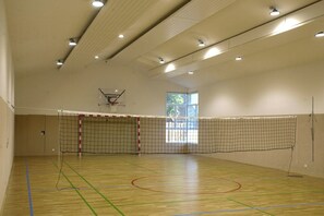 Une salle de sport équipée d’un terrain de basket-ball, d’un filet de volley-ball et d’un panier de basket.