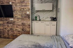 A compact room with a bed, a small kitchenette with a sink, and a mounted television. - Free Parking · Private Studio with Terrace (Herzliya)