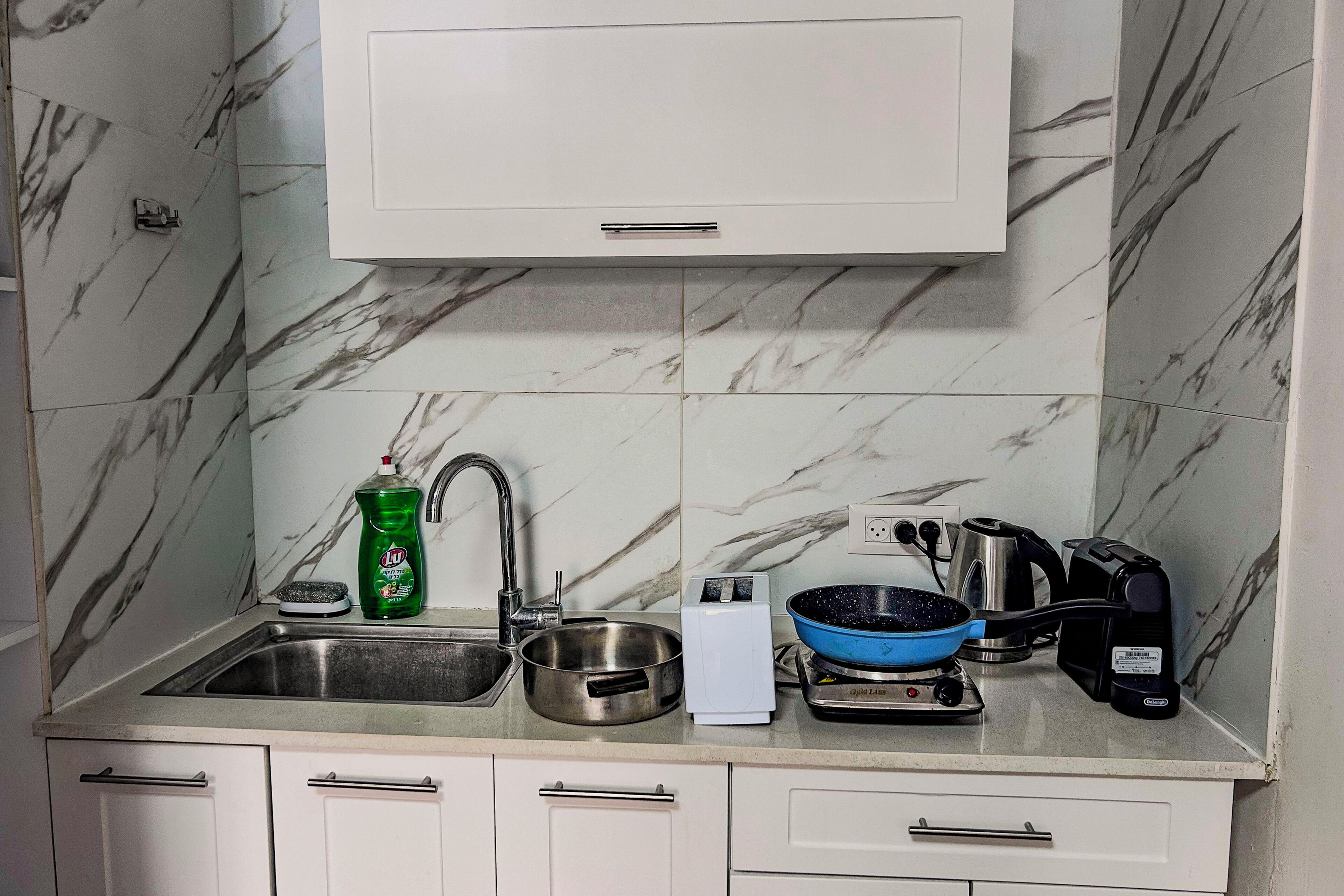 Una cocina con un lavamanos, una botella de detergente, una tetera y una sartén sobre la encimera.