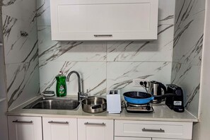 A kitchen with a sink, a dish soap bottle, a kettle, and a frying pan on the counter.