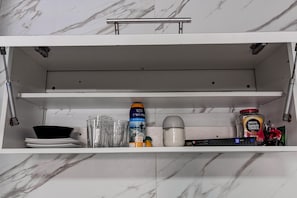 Ein Küchenschrank mit Regalen, der verschiedene Gegenstände wie eine Dose, ein Glas, ein Messbecher und Gläser enthält.