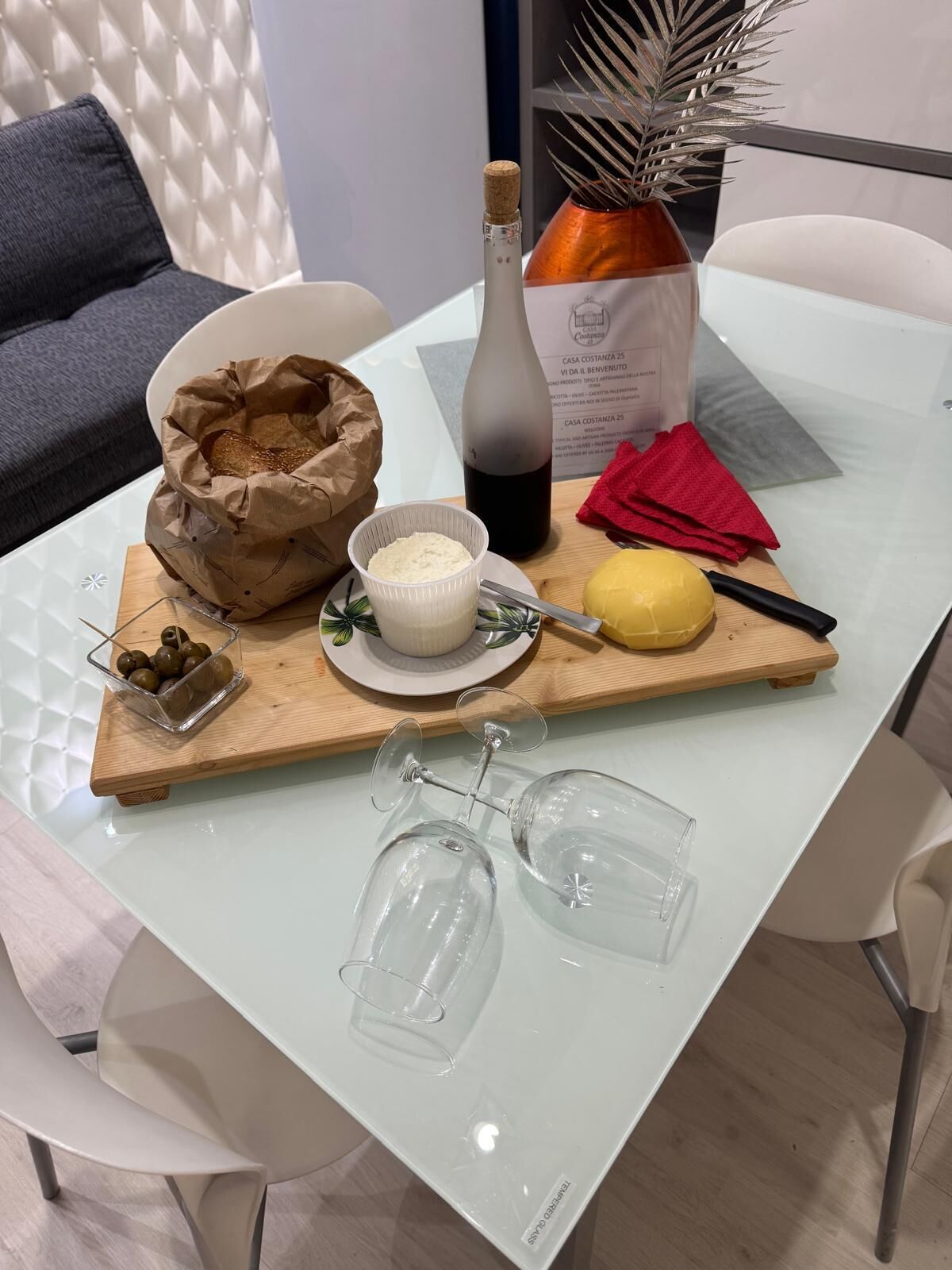 A dining table with a bottle, a bowl of food, a yellow fruit, and a pair of glasses.