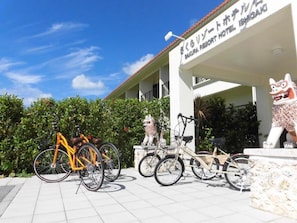 Entrada de hotel con un letrero, una estatua y bicicletas estacionadas.