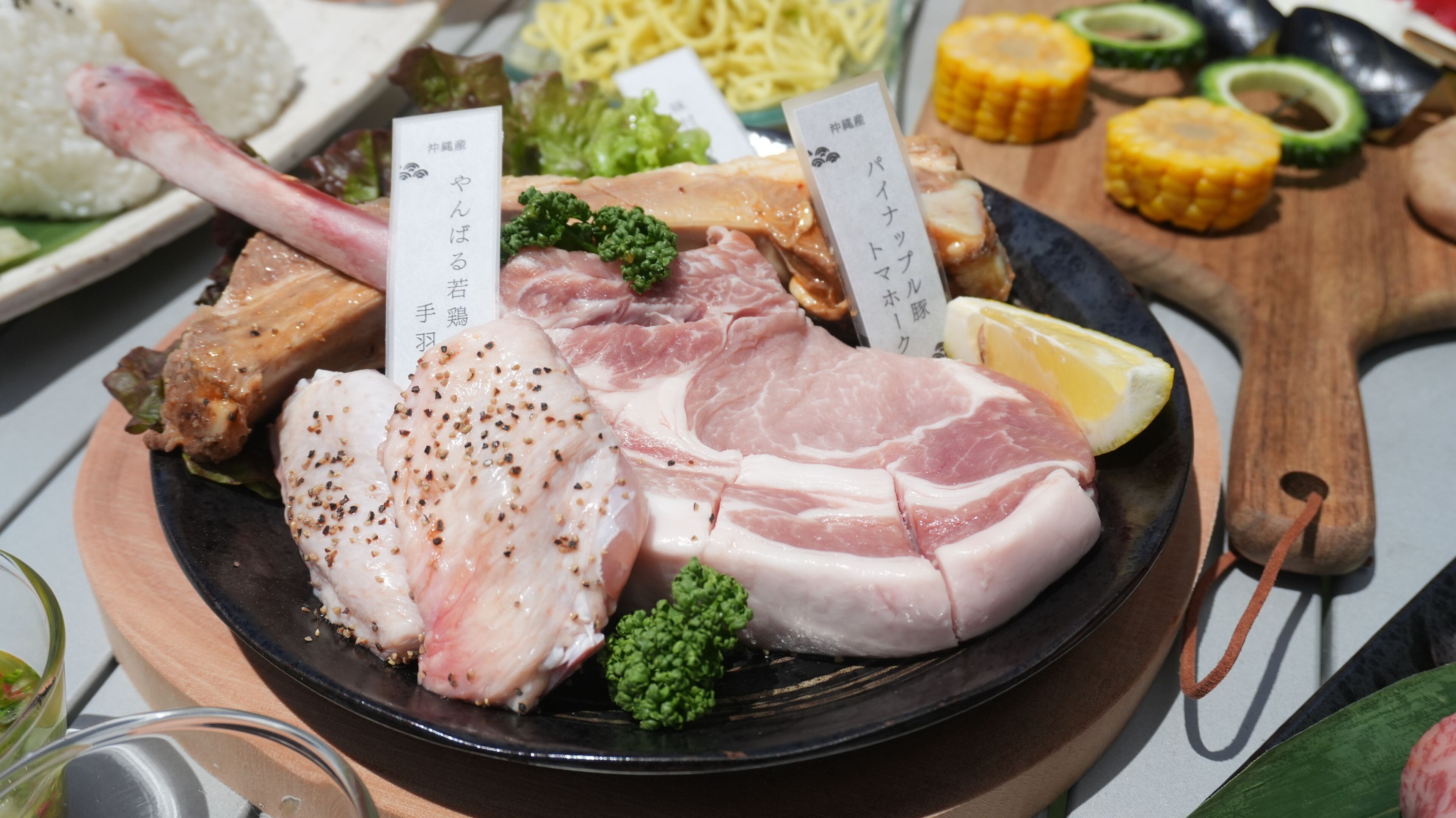 A variety of raw meats on a plate with labels, accompanied by vegetables and a lemon wedge.