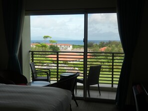 Une chambre d’hôtel avec un balcon, un lit, deux chaises et une petite table.