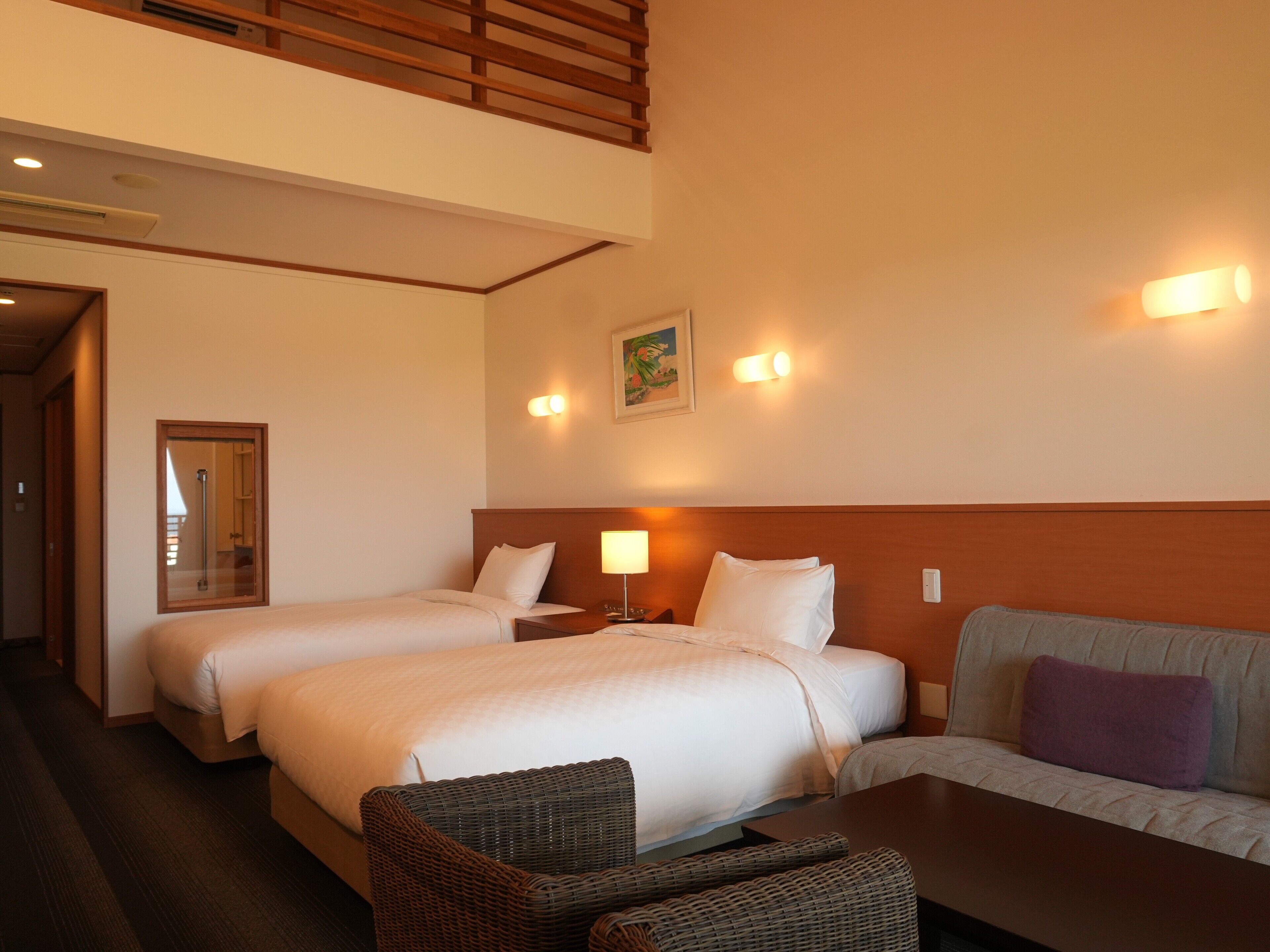 A hotel room with two beds, a sofa, a table, and a mirror.