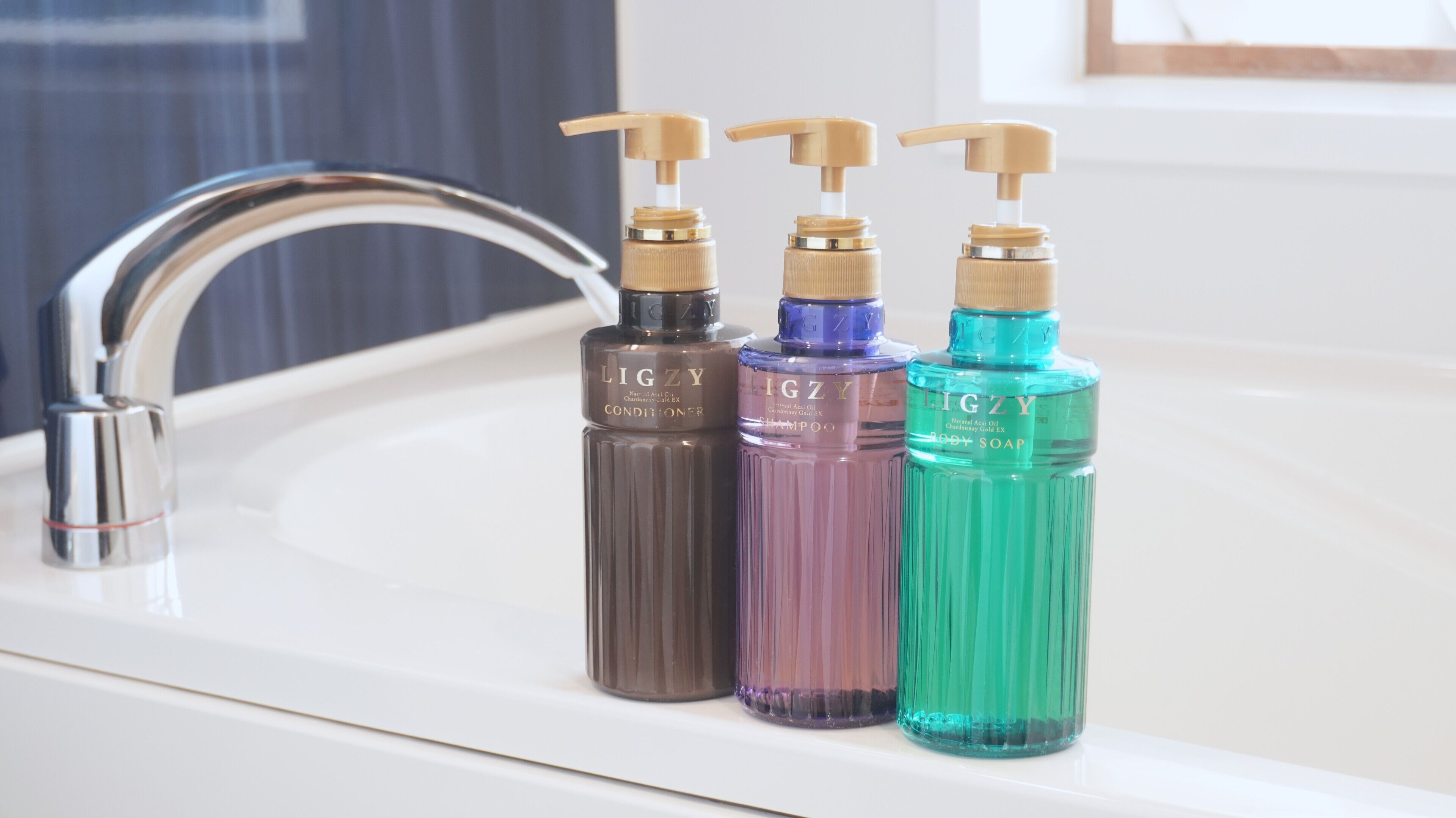 A bathroom sink with three bottles of body soap.