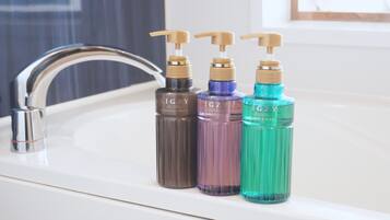 A bathroom sink with three bottles of body soap.