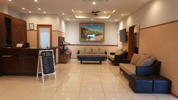 A hotel lobby with a reception desk, seating area, and a large painting on the wall.