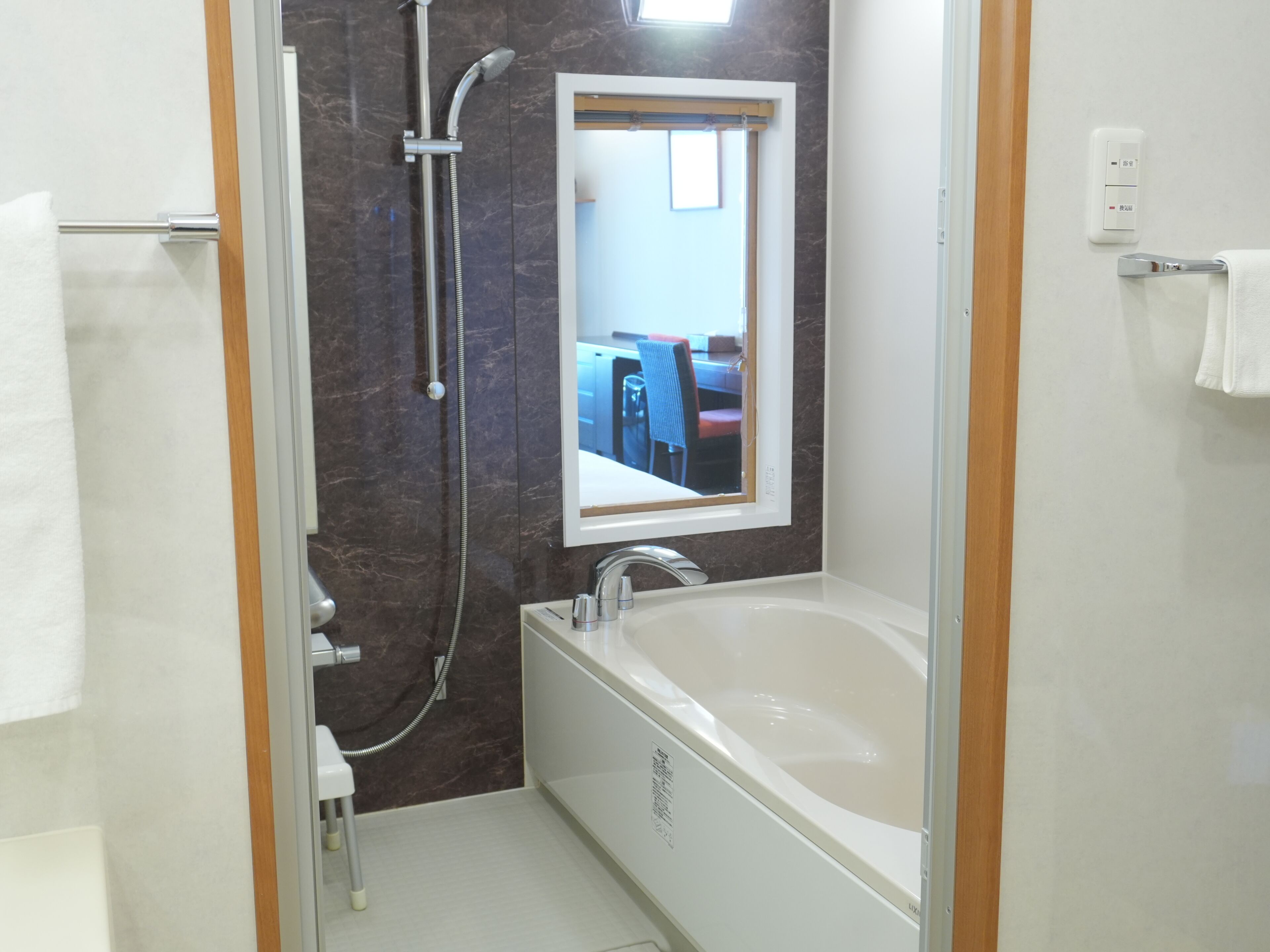 Baño con bañera, ducha y espejo que refleja un comedor.