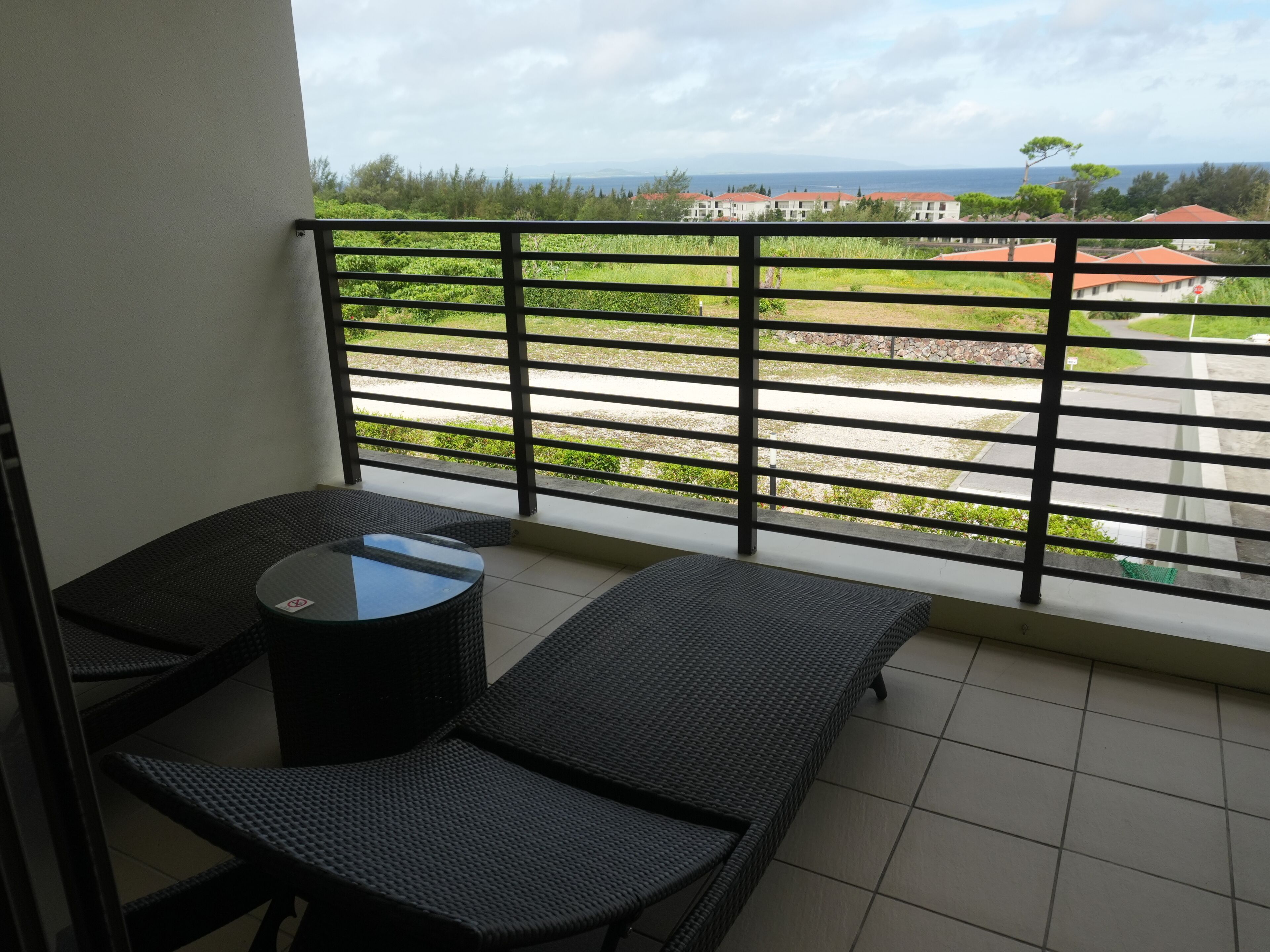 A balcony with a view of a road, greenery, and distant buildings.