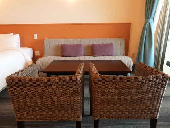 Una habitación de hotel con cama, dos sillas, una mesa y un sofá con cojines.