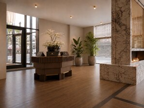 A modern lobby with a reception desk, potted plants, and a fireplace. - Hotel AMANO München Stachus (Munich)