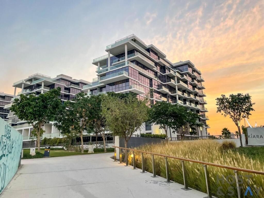 A multi-story residential building with balconies, a paved walkway, and greenery.