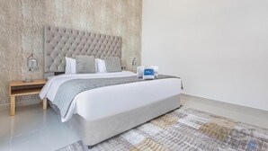 A modern hotel room with a tufted headboard, a neatly made bed, a bedside table with a lamp, and a digital clock. - Orchid A Damac Hills - Host & Stay (Dubai)