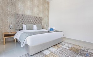 Ein modernes Hotelzimmer mit einem gesteppten Kopfteil, einem ordentlich bezogenen Bett, einem Nachttisch mit Lampe und einer digitalen Uhr.
