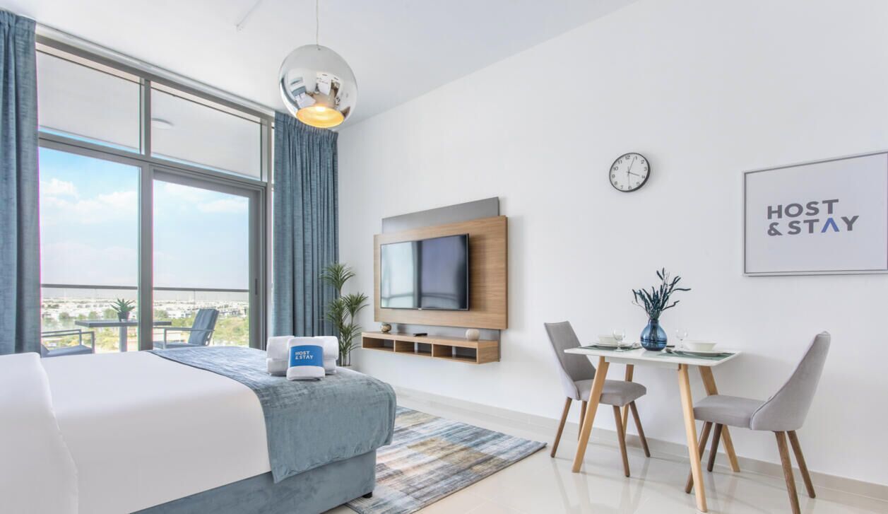 A modern hotel room with a large bed, a dining table, a TV, and a balcony with a view.