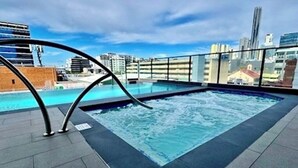 Ein Pool auf dem Dach mit Blick auf die Stadt, umgeben von einem Glasgeländer.