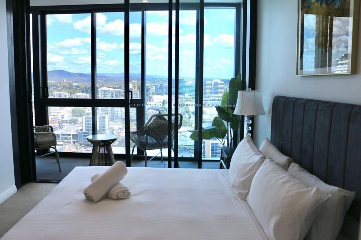 Ein Hotelzimmer mit einem großen Bett, Blick auf die Stadt, einem Sessel und einem Tisch.
