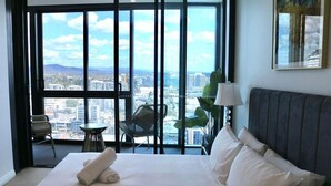 Ein Hotelzimmer mit einem großen Bett, Blick auf die Stadt, einem Sessel und einem Tisch.