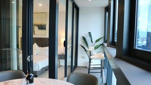 Ein modernes Hotelzimmer mit einem Bett, einer Sitzecke mit Sessel und Tisch sowie einem Balkon mit Pflanze.