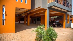 A building with a covered entrance, a car parked in front, and a landscaped area with plants. - Izera Suites (Kampala)
