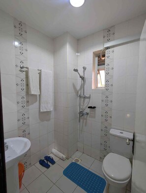 Un baño con ducha, inodoro, lavamanos y ventana.
