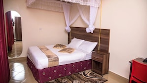 A hotel room with a bed, a nightstand, a bedside table, a mirror, and a red chair. - Izera Suites (Kampala)