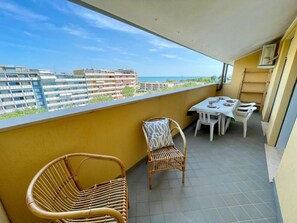 Ein Balkon mit Tisch und Stühlen, ein Korbstuhl und Blick auf Gebäude und das Meer.