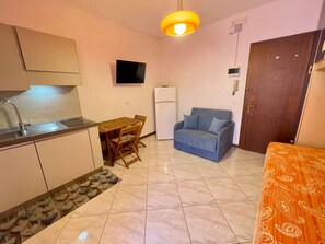 A compact living space with a kitchenette, a dining area, a sofa, and a patterned bedspread. - Practical studio with balcony by the beach (Porto Santa Margherita)