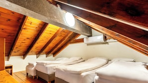 Ein Zimmer mit schrägen Wänden, Holzbalken und einem Bett mit weißer Bettwäsche.