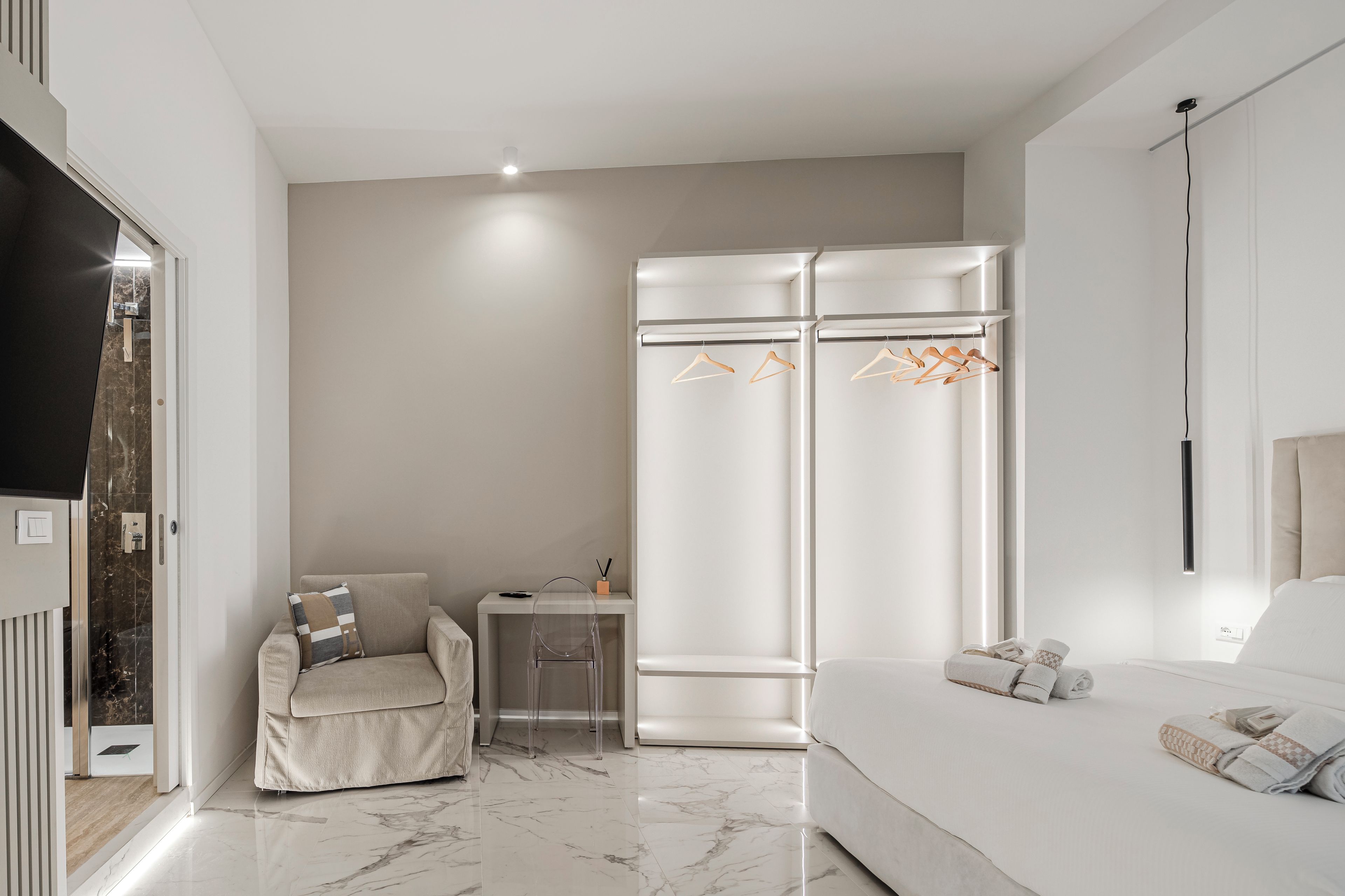 A modern bedroom with a sofa, a chair, a wardrobe, and a small table with a lamp.
