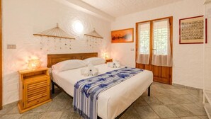 Ein Schlafzimmer mit einem Holzbett, zwei Nachttischen, einem Beistelltisch, einem Fenster mit Vorhängen und einer Wandlampe.