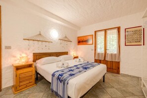 Ein Schlafzimmer mit einem Holzbett, zwei Nachttischen, einem Beistelltisch, einem Fenster mit Vorhängen und einer Wandlampe.