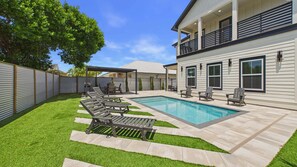 Ein Garten mit Swimmingpool, Sitzgelegenheiten im Freien und einer überdachten Terrasse.