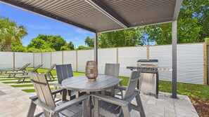 Eine Terrasse im Freien mit einem runden Tisch, Stühlen, einem Grill und einer dekorativen Vase.