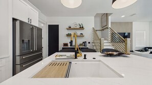 A modern kitchen with a stainless steel refrigerator, a white countertop, and a gold faucet.