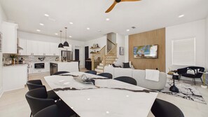 Una cocina moderna con armarios blancos, una isla central y un comedor con mesa de mármol y sillas negras.