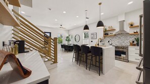 A modern kitchen with a central island, bar stools, and a staircase with wooden railings.