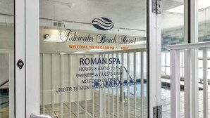 En glasdörr med en skylt som visar information om Tidewater Beach Resorts romerska spa, öppettider och åldersgränser.