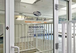 Eine Glastür mit Schild für das römische Spa des Tidewater Beach Resort, Öffnungszeiten und Altersbeschränkungen.