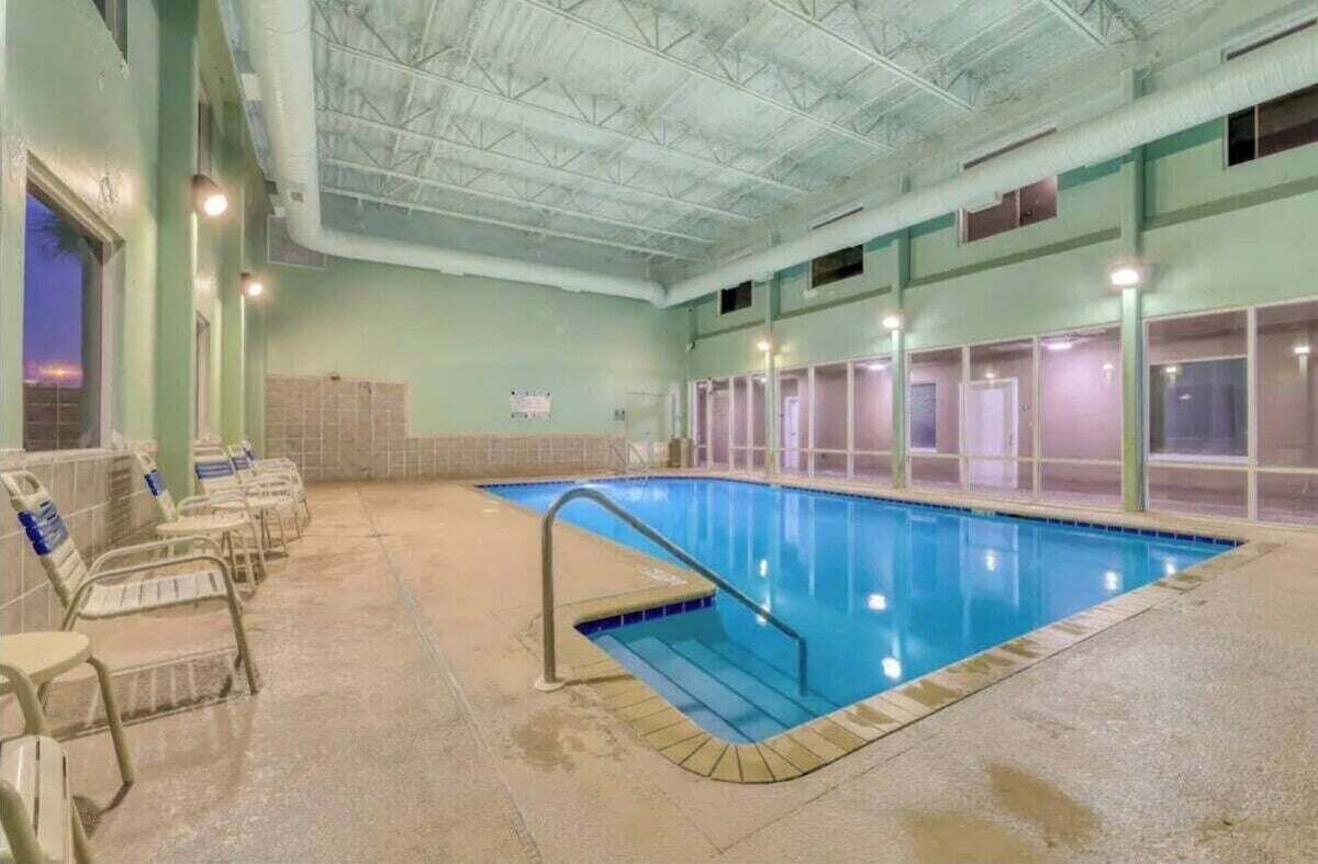 Ein Hallenbad mit gefliestem Boden, einer Metalltreppe und mehreren Stuhlreihen entlang der Wände.