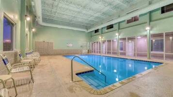 Piscina interior com chão de azulejos, escada de metal e fileiras de cadeiras ao longo das paredes.