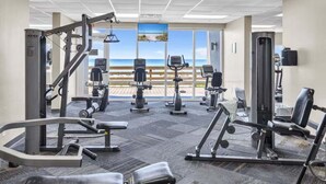 Ett gym med konditionsmaskiner, utrustning för styrketräning och utsikt över stranden.