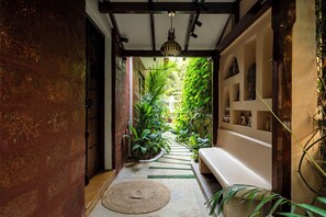 Un pasillo estrecho con una puerta de madera, una pared de piedra, un aplique colgante y una pared cubierta de plantas verdes.