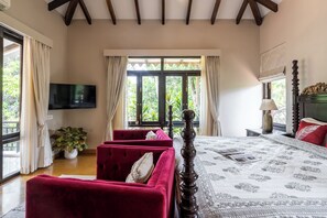 Un dormitorio con una cama grande, televisión, ventana con cortinas y sofá rojo.