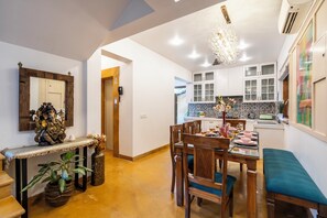 Un comedor con una mesa de madera, sillas y un banco. Se observa una cocina al fondo con armarios blancos y un salpicadero de azulejos.