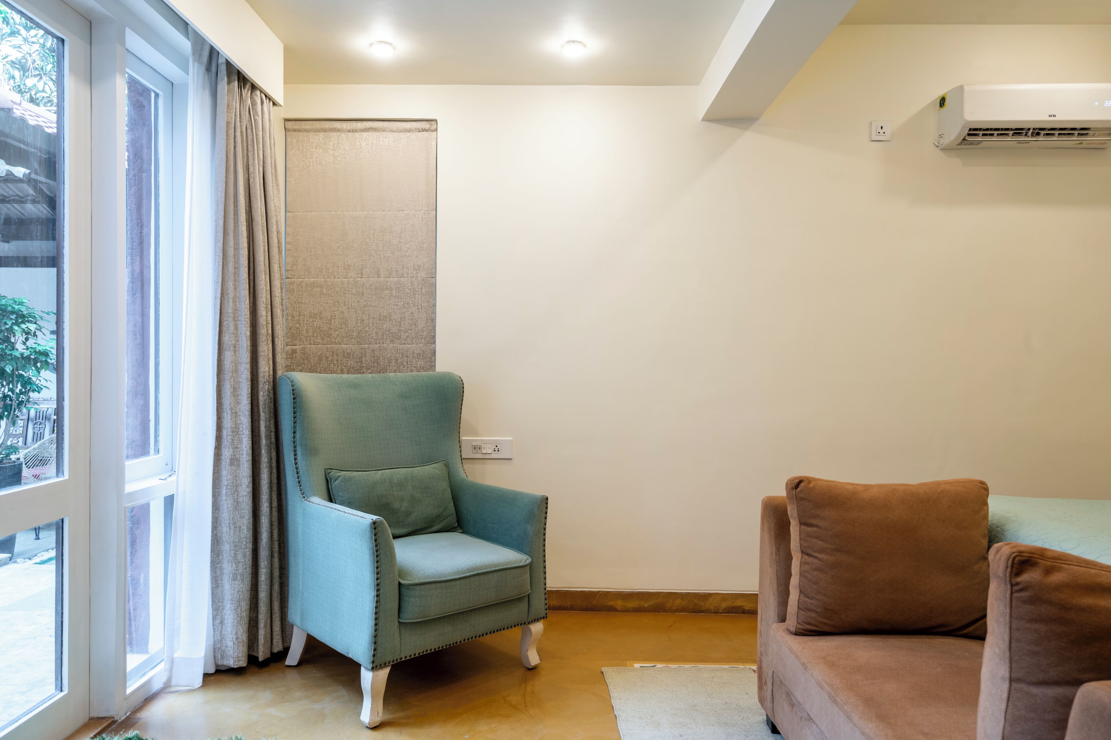A room with a window, a chair, a couch, and an air conditioning unit.