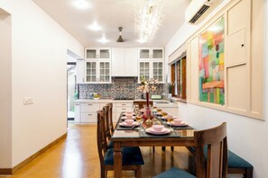 A modern kitchen with white cabinets, a tiled backsplash, and a dining area set for a meal. - Staymaster Shangrila-4BR Private villa  (Marra)