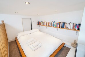 A neatly made bed with white linens and towels, a wooden headboard, a bookshelf with various books, and a simple, clean room design. - Perfect apartment in London close to top attractions and nightlife (London)